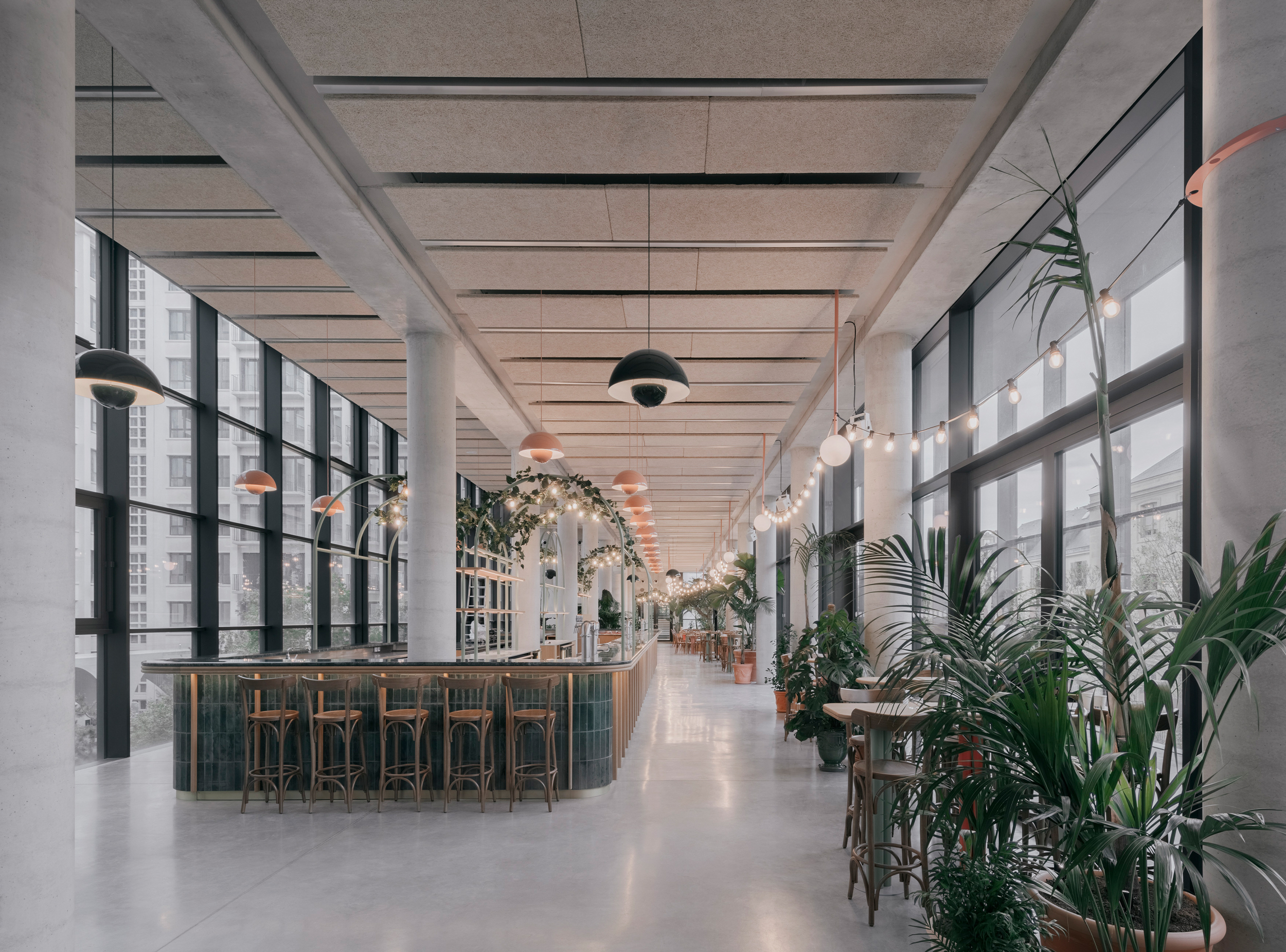 Interior of the youth hostel bar, located above the public arcade between Boulevard Morland and the courtyard, with generous glazing, planting and communal seating.