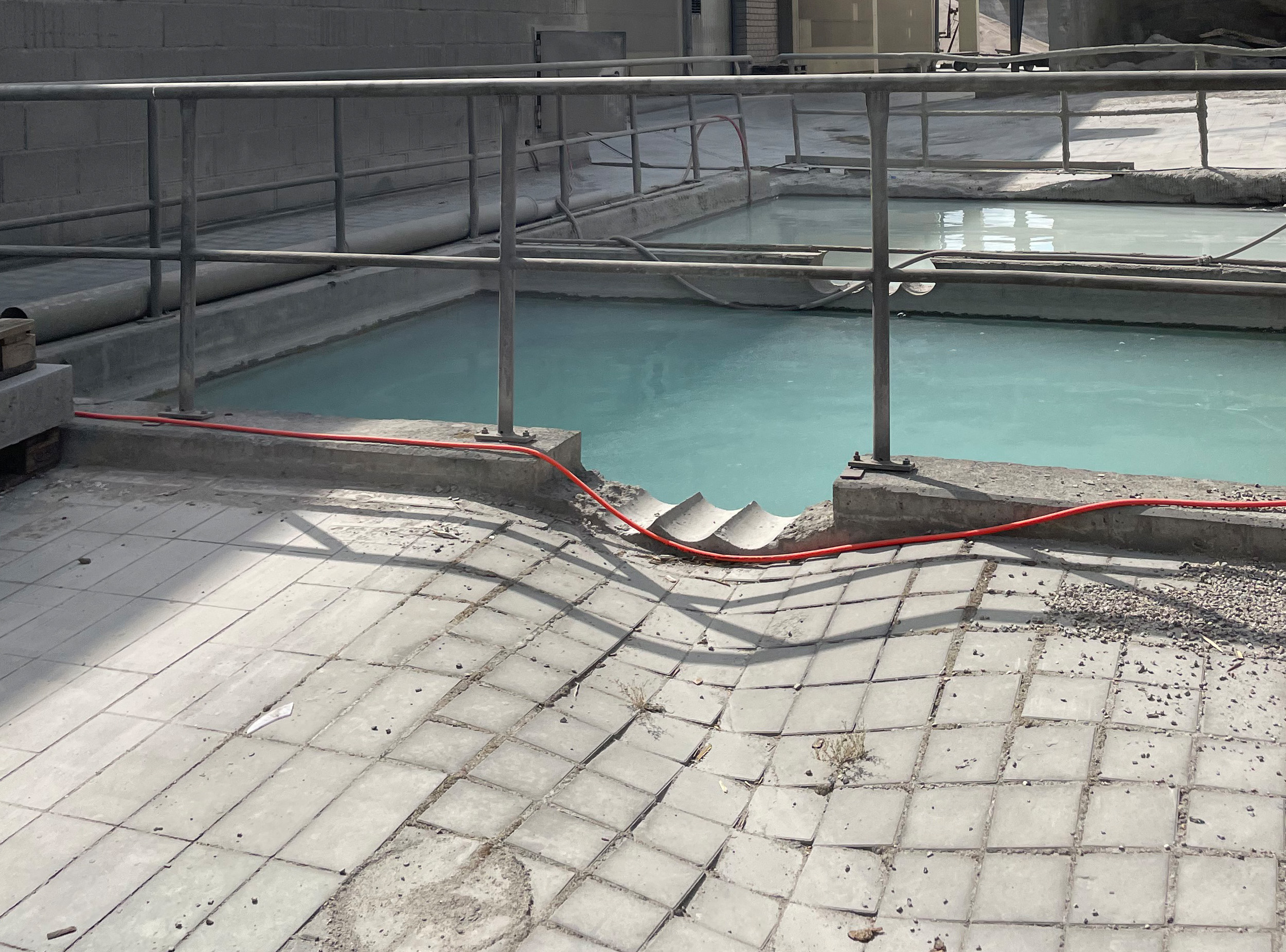 Existing precast concrete paving forming an unexpected curved surface beside water basins at a production site for concrete paving stones.