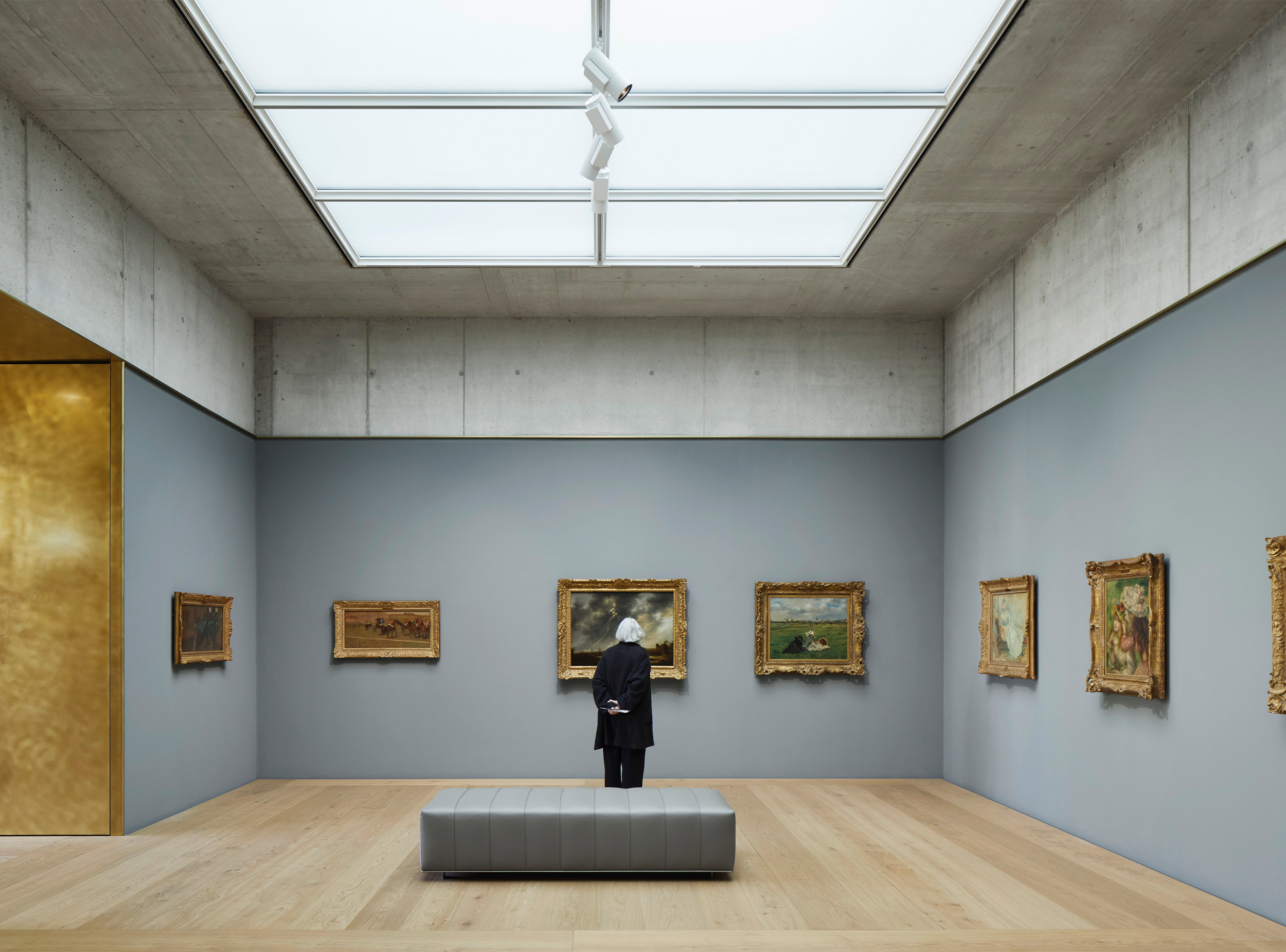 A gallery of the Kunsthaus Zürich Extension is defined by exposed concrete surfaces, timber floors and a large diffuse skylight that provides controlled natural illumination, creating a serene and carefully proportioned environment for the appreciation of art.