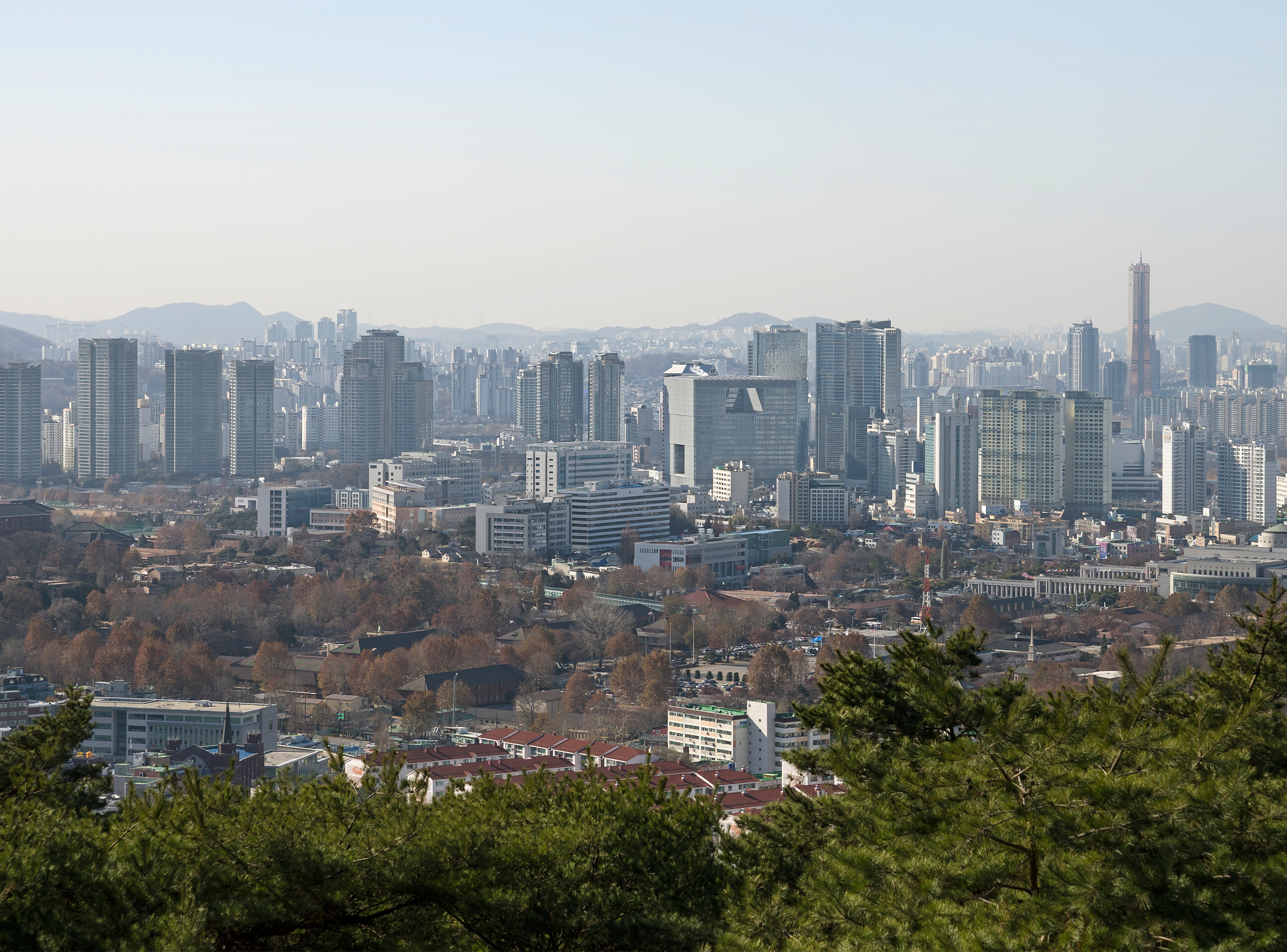View across Seoul’s Yongsan district showing the Amorepacific headquarters among the city’s skyline, with parkland in the foreground and mountains beyond.