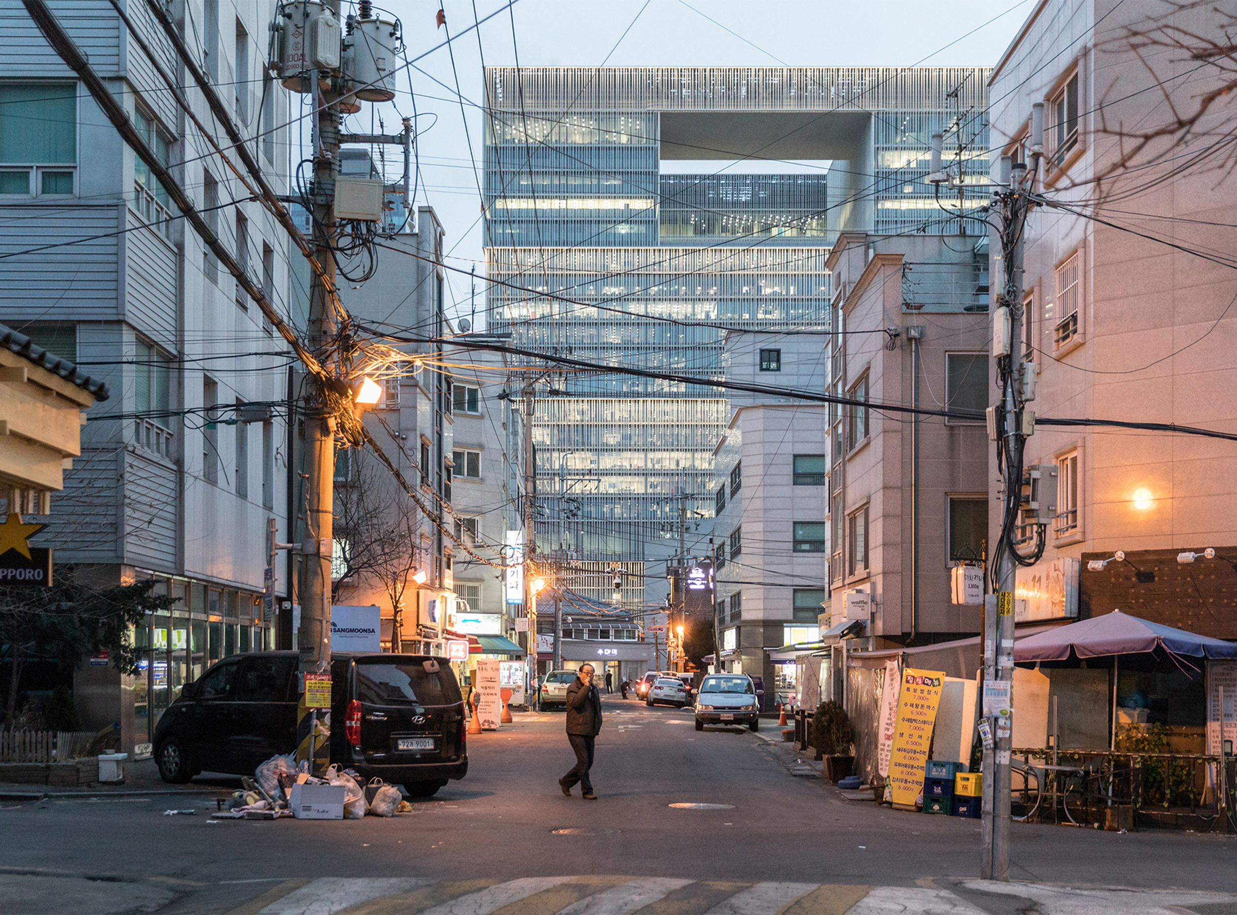 Evening view along a local street in Seoul with the Amorepacific headquarters illuminated in the distance.