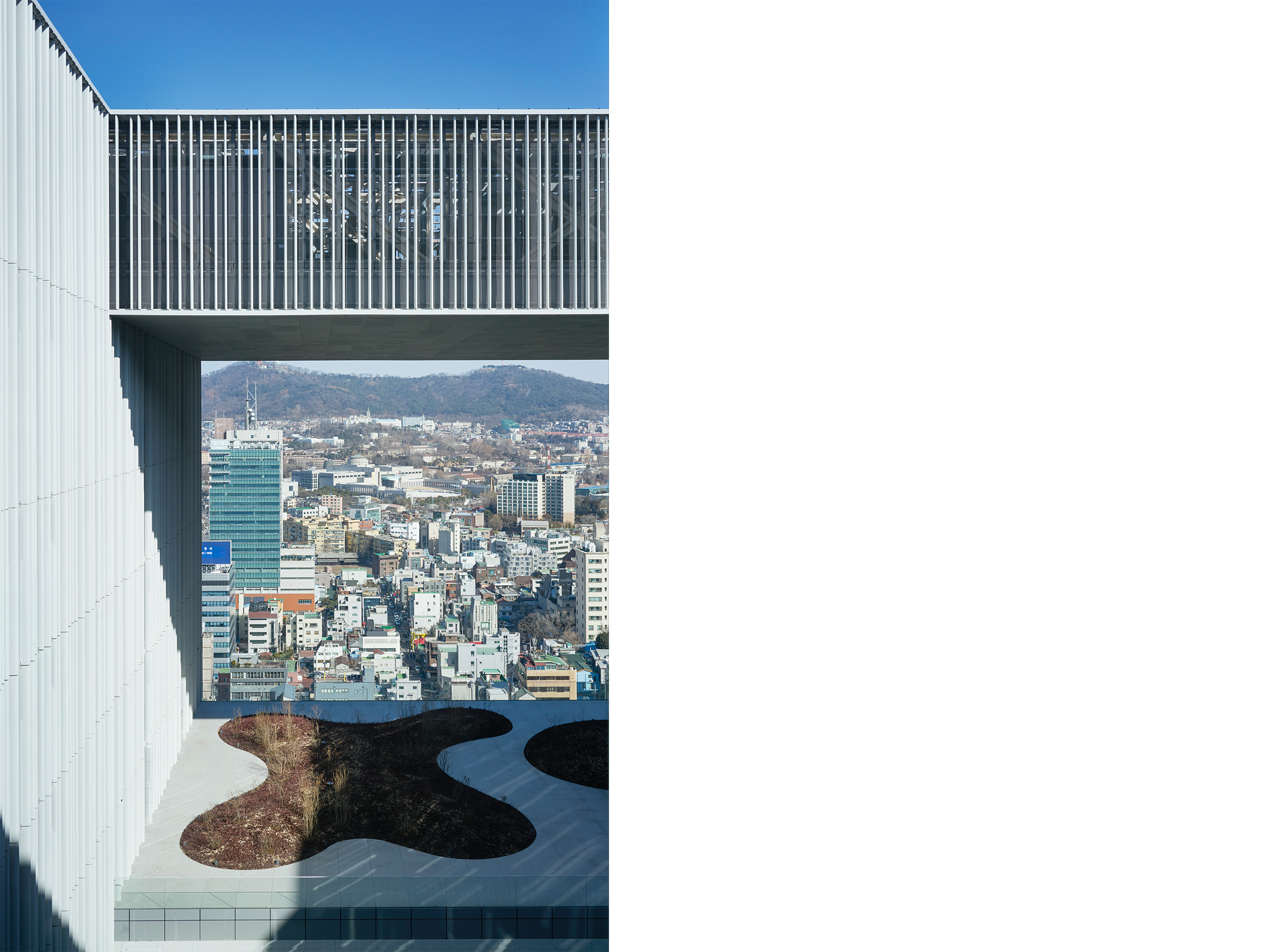 Framed view from one of the Amorepacific headquarters’ elevated garden openings towards the Seoul skyline and surrounding hills.