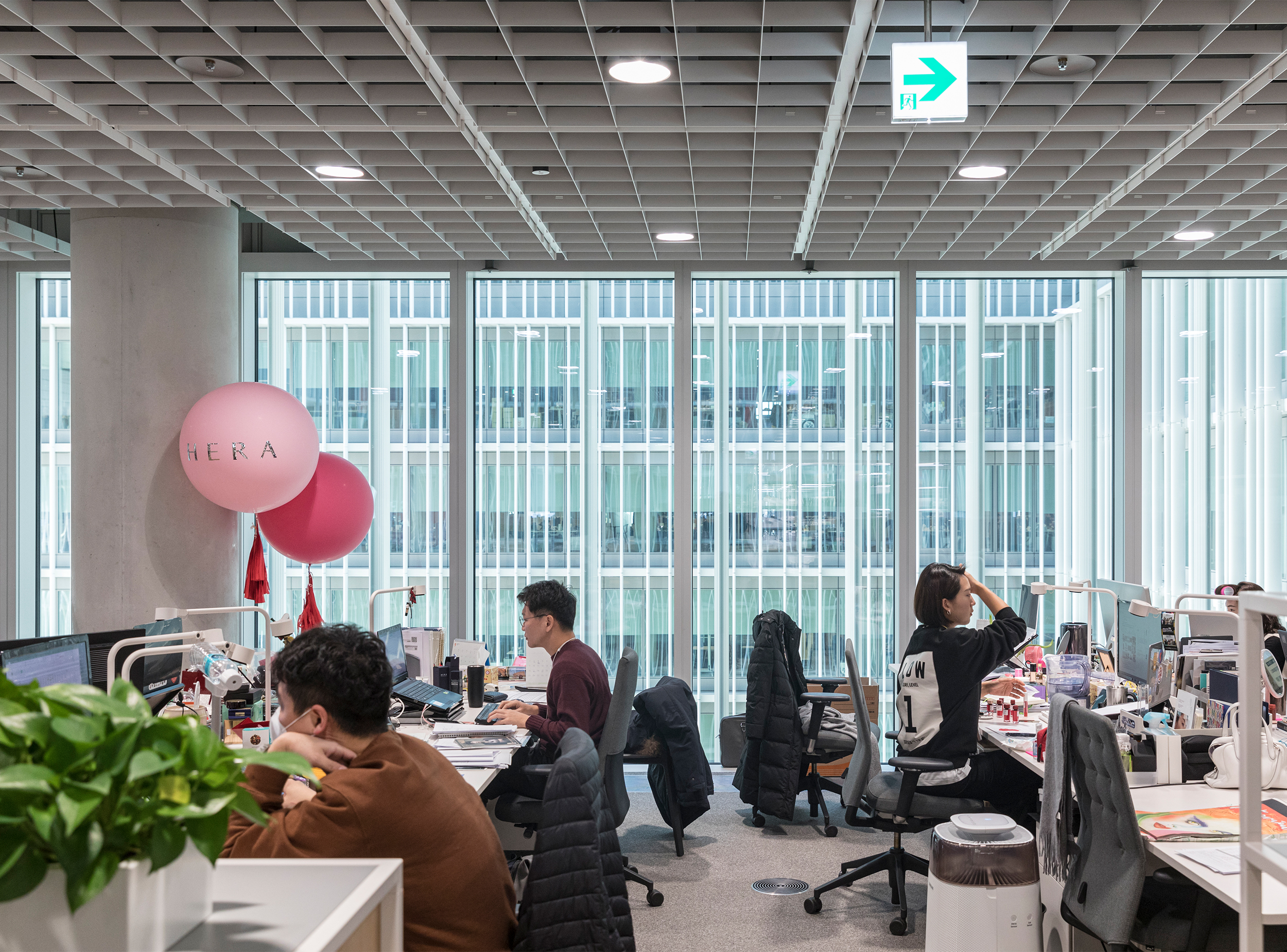Open-plan office space within the Amorepacific headquarters, with workstations arranged along a glazed façade overlooking the central courtyard.